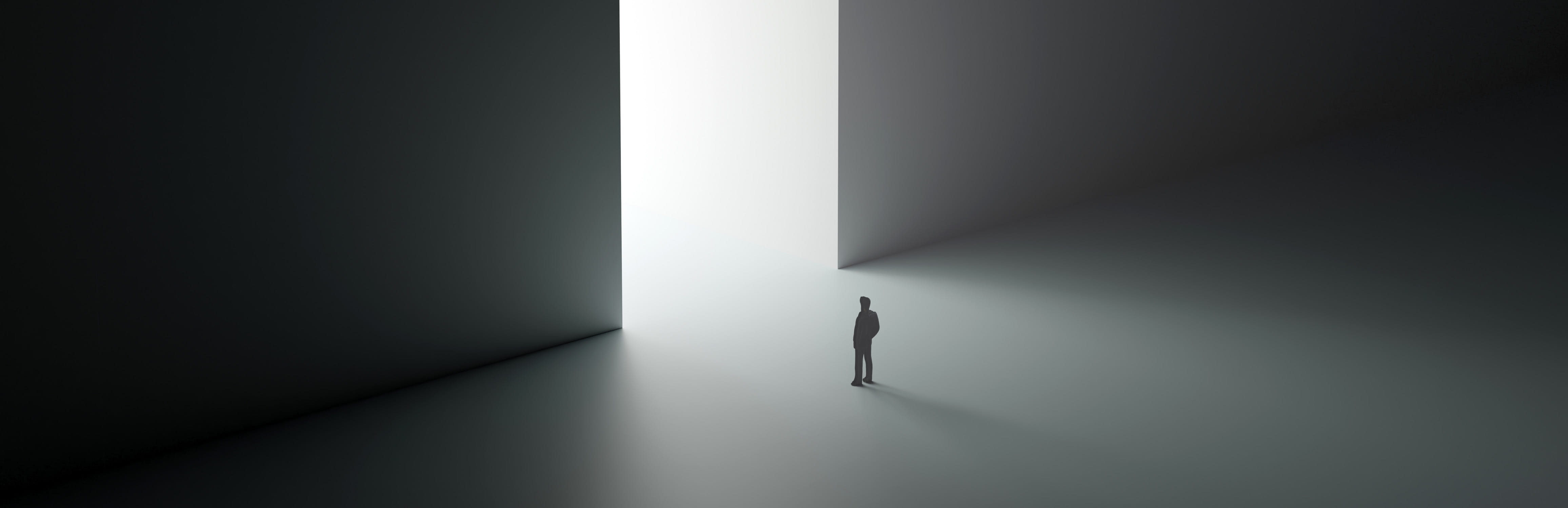 Silhouette of a person standing before a towering, bright doorway in a dark, minimalist space.